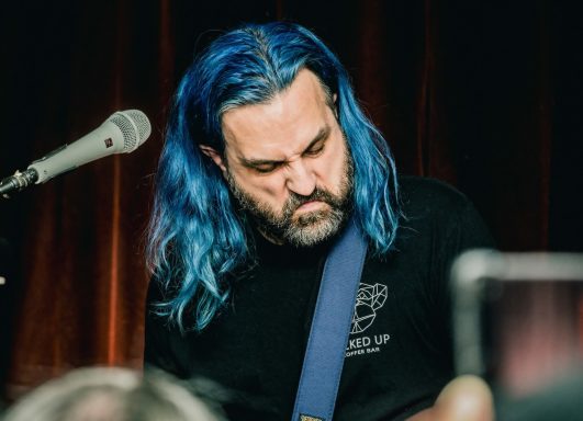 Rouge Pompier - Radiothon CKRL 89,1 Musician with blue hair playing guitar on stage, focused on performance.
