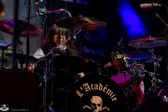 Drummer performing on stage with colorful lights and a bass drum featuring a logo.