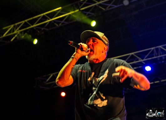 A male performer raps on stage with colorful lights in the background.