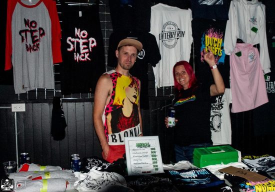 Merchandise booth featuring two people with t-shirts and colorful designs on display.