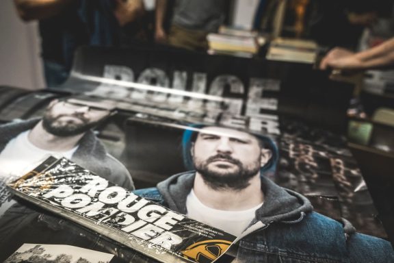 Rouge Pompier - Radiothon CKRL 89,1 Posters featuring a man in a hoodie and text reading "Rouge Poumier" on a table.