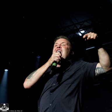 Man singing passionately into a microphone on stage with dramatic lighting.