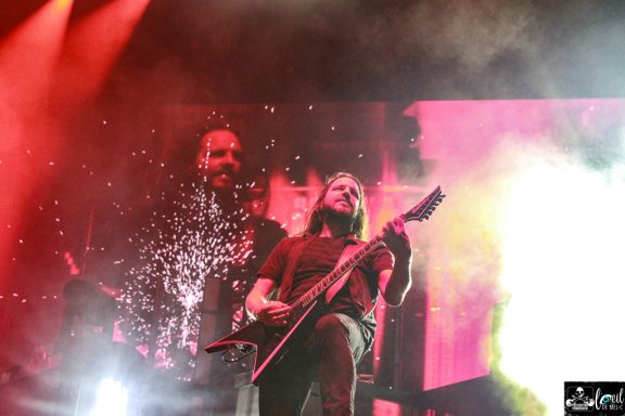 A guitarist performs on stage with vibrant lighting and background visuals.