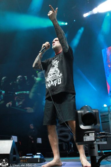 A performer singing on stage, wearing a black t-shirt and shorts, with dramatic lighting.