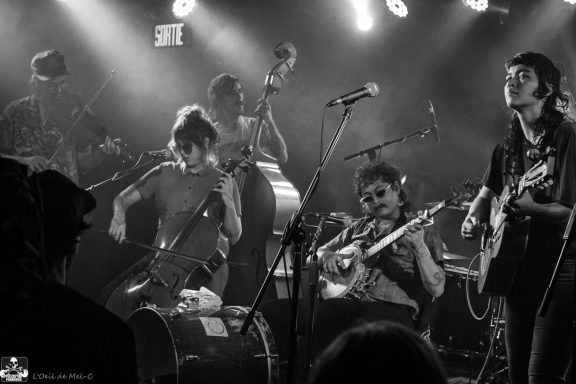 Black and white scene of a band performing with various instruments on stage.