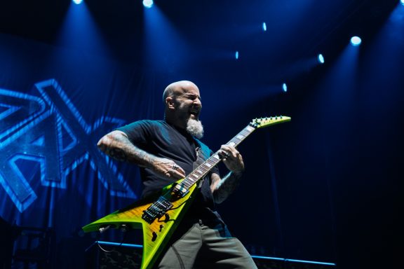 Musician playing a bright yellow guitar on stage with dramatic blue lighting.