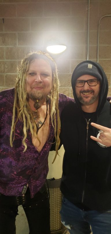 Two men posing together, one with long dreadlocks and a purple shirt, the other in a black hoodie.