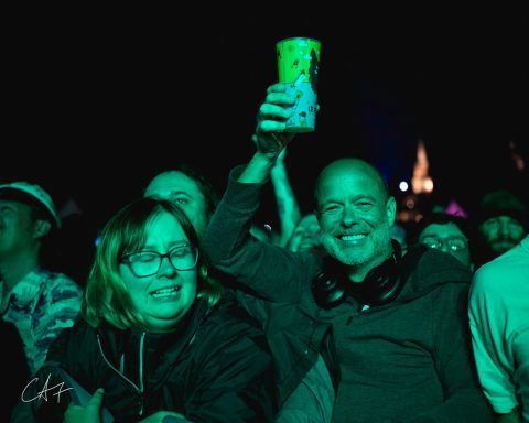 Crowd enjoying a concert, with a person holding a drink and smiling.