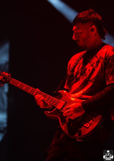 Musician playing electric guitar on stage with dramatic lighting.