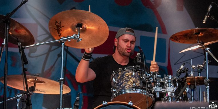 Drummer performing on stage with a focused expression and drumsticks in hand.