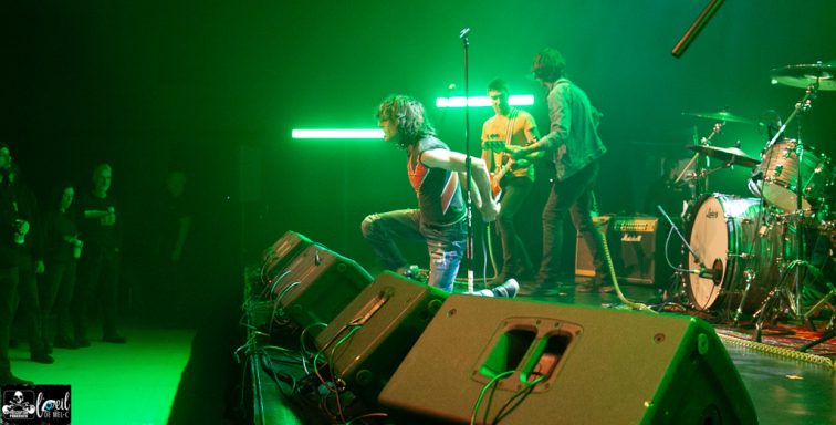 A band performing on stage with green lighting, energetic audience in front.
