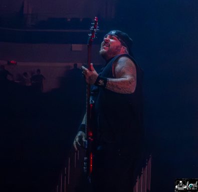 A musician playing the bass guitar on stage with dramatic lighting.