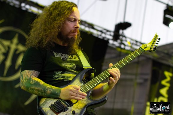 Man with long curly hair playing an electric guitar on stage.