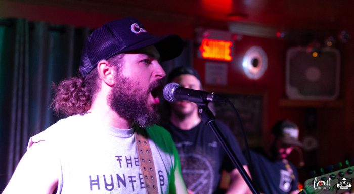 Male musician singing into a microphone while performing on stage.