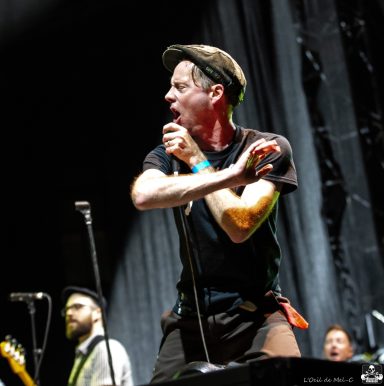 Lead singer performing energetically on stage, with band members in the background.