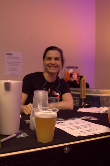 Person smiling behind a bar with glasses and drinks in front.