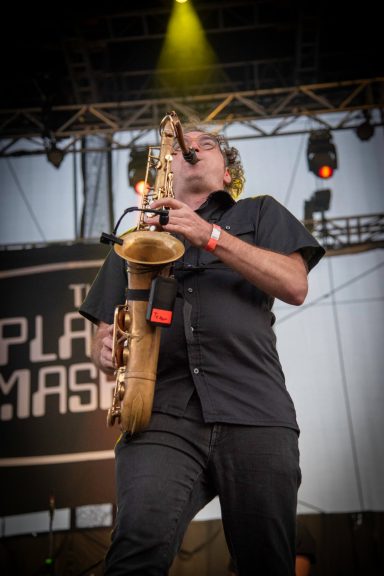 Musician playing saxophone on stage with performance lights in the background.