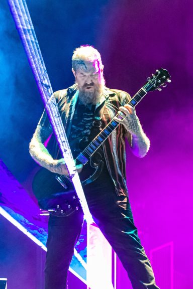 Musician playing electric guitar on stage with colorful lighting.
