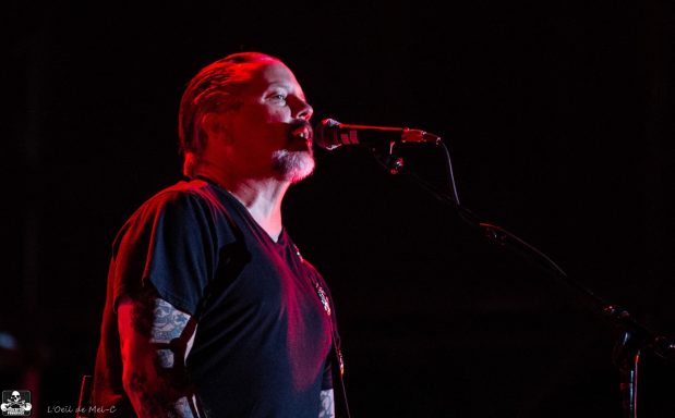 Musician singing into a microphone with dramatic lighting on stage.