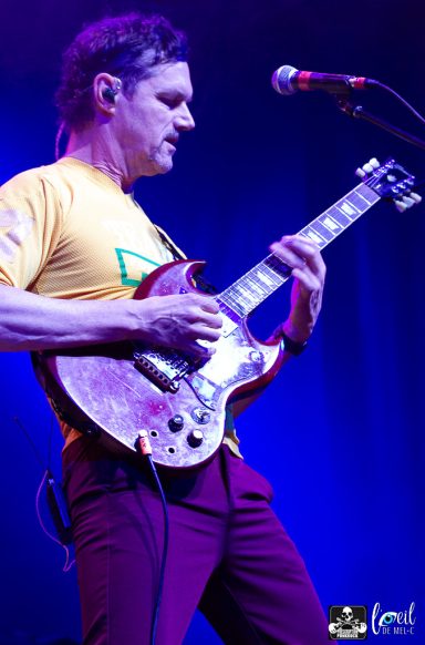 Musician playing electric guitar on stage with colorful lighting.