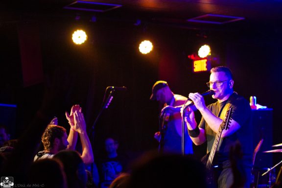 A band performs on stage, with fans cheering in a dimly lit venue.