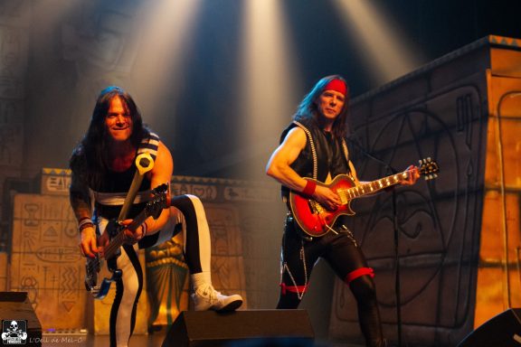 Two musicians perform on stage, one playing bass and the other guitar, with vibrant lighting.