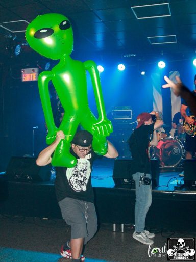 A person carrying a large green alien figure at a concert venue.