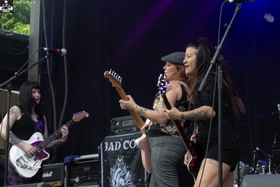 A female band performing live on stage with instruments and energetic expressions.