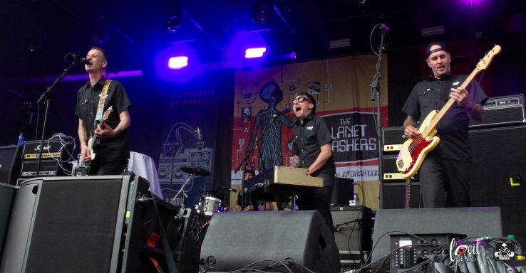 Three musicians performing on stage with instruments, illuminated by purple stage lights.