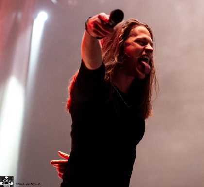 A musician performing passionately on stage, with long hair and a microphone.