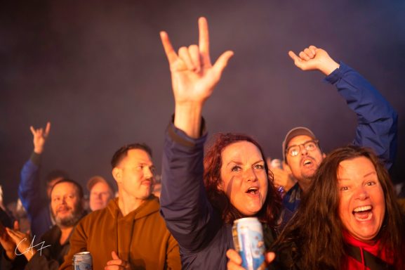 Crowd at a concert celebrating with hands raised and smiling faces.