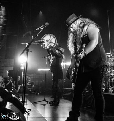 Two musicians performing on stage with guitars, illuminated by stage lights.