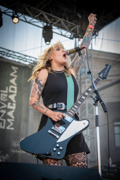 Female guitarist with tattoos performing enthusiastically on stage.