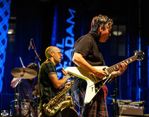 Musicians performing on stage, one playing guitar and another on saxophone.