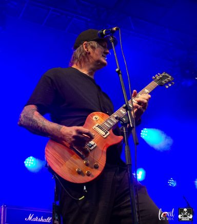 Musician playing electric guitar on stage with blue lighting.