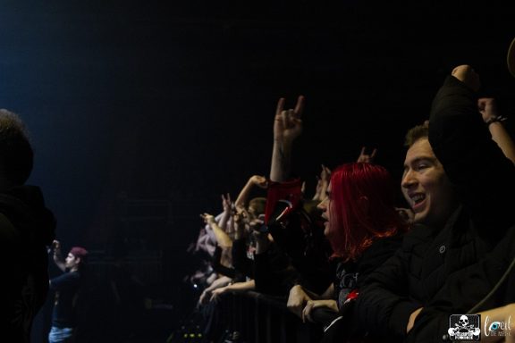 Crowd at a concert, some fans cheering and raising their hands in excitement.