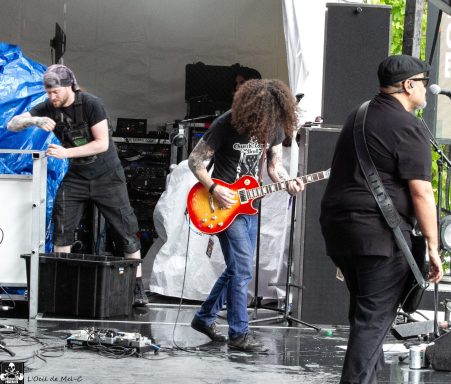 Band members performing on stage, with one guitarist playing a bright red electric guitar.