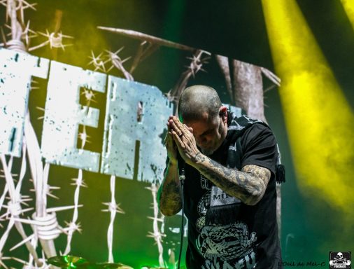 Musician on stage with hands clasped in prayer, illuminated by yellow stage lights.