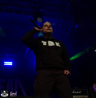 A performer on stage holds a microphone, wearing a black hoodie with "TDE" printed on it.