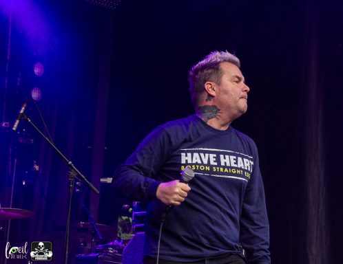 A man singing on stage, wearing a "Have Heart" sweatshirt.