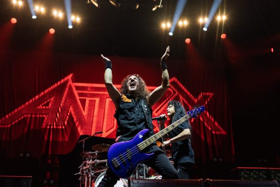 Band members performing on stage with energetic poses and bright stage lights.