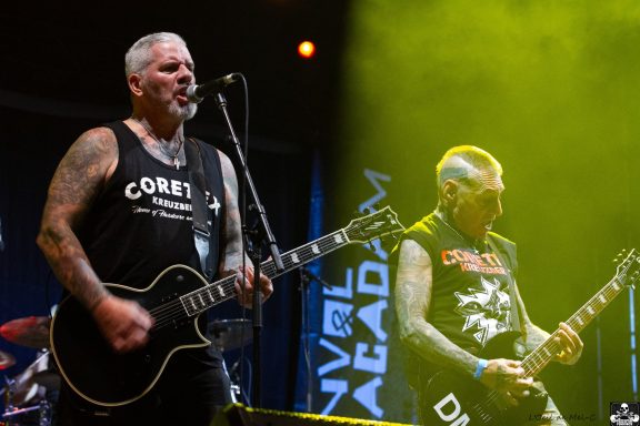 Two tattooed male musicians performing on stage with electric guitars.