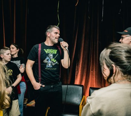 Pépé et sa guitare - Radiothon CKRL 89,1 A man in a black shirt speaking to a group of people at an event.