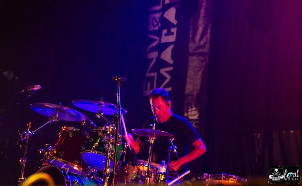 Drummer performing on stage with vibrant lighting and a backdrop banner.