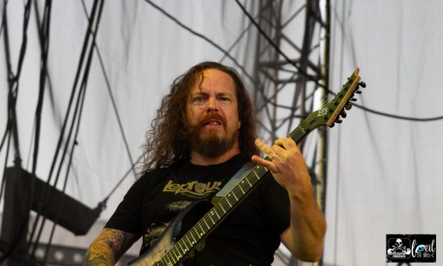 Musician with long hair playing an electric guitar on stage.