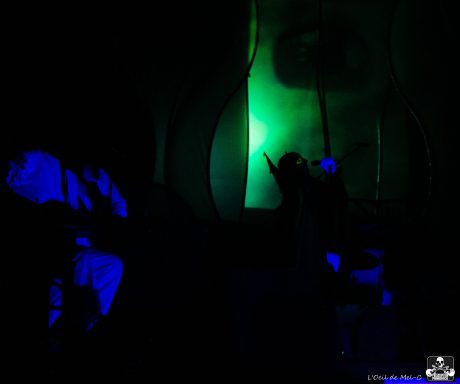 A figure in dark surroundings illuminated by blue and green lights.