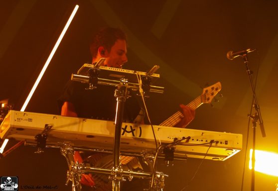 Musician playing keyboard and guitar on stage with dramatic lighting.