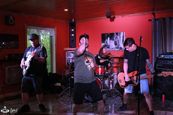 A rock band performs on stage in a vibrant, orange-walled venue.