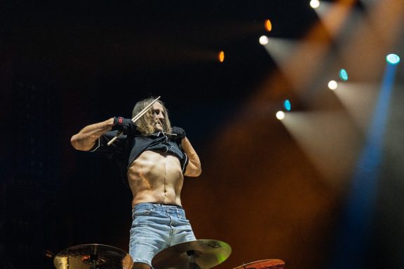 Rock musician performing passionately on stage, revealing a toned physique.