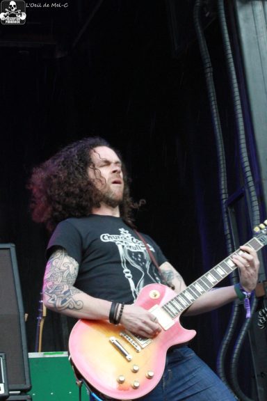 A guitarist with curly hair passionately playing an electric guitar on stage.